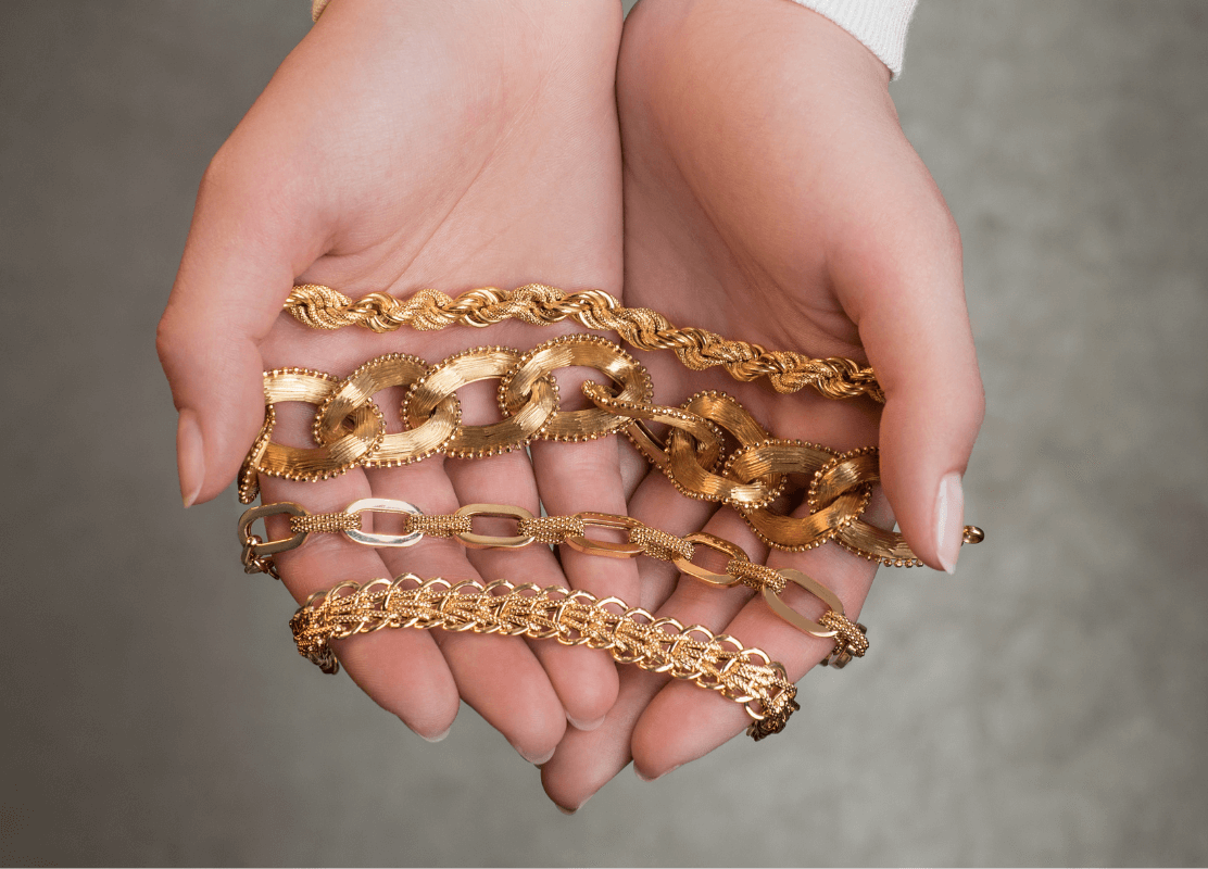 Četiri zlatne lančane narukvice elegantno prikazane u paru ruku.