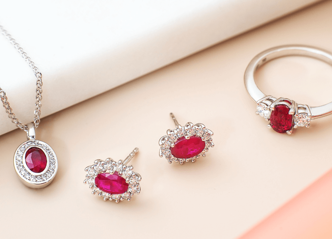 white gold jewelry with diamonds and rubies on pink background
