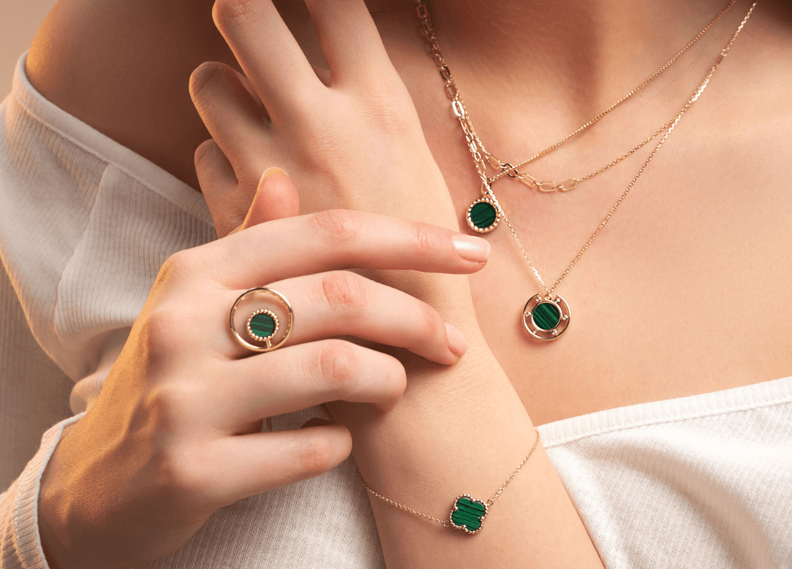 Žena koja nosi prekrasnu ogrlicu i prstenje od zelenog kamena malahita, dodajući dašak elegancije svojoj odjeći.