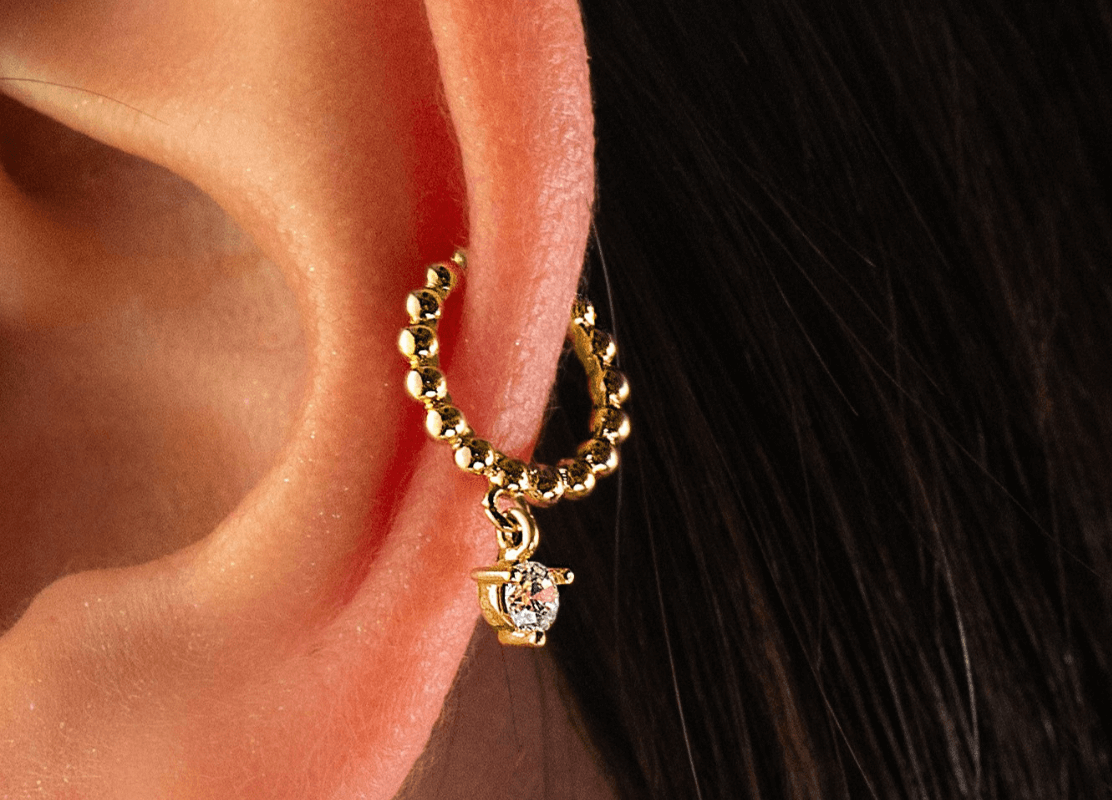 zlatna naušnica earcuff uz detalj cirkona na ženskoj osobi