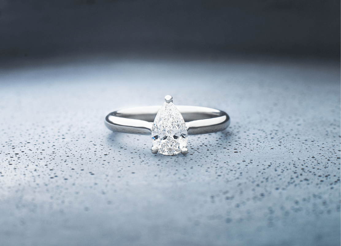 Sjajni dijamantni prsten od platine u obliku kruške, na čistoj pozadini.