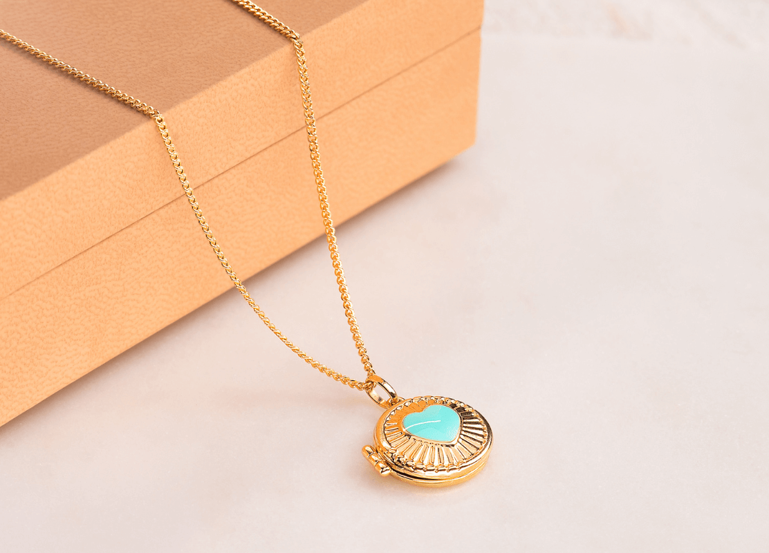 Zlatna ogrlica s okruglim privjeskom u obliku medaljona s tirkiznim privjeskom u obliku srca, savršen za dodavanje daška boje svakoj odjeći.