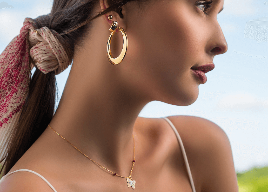 Slika mlade žene ukrašena Dodić zlatnim nakitom savršenim za ljetni ten, ogrlicom i naušnicama.
