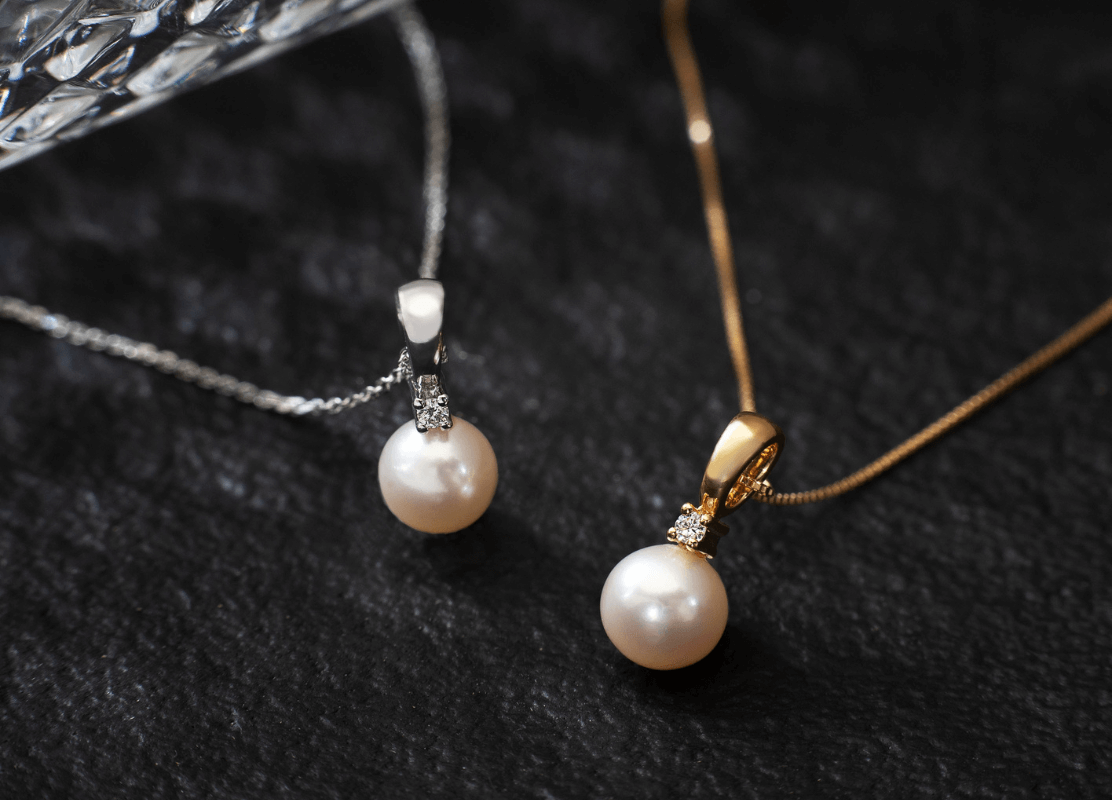 Dvije elegantne zlatne ogrlice s biserima na glatkoj crnoj površini, odišu sofisticiranošću i bezvremenskom ljepotom.