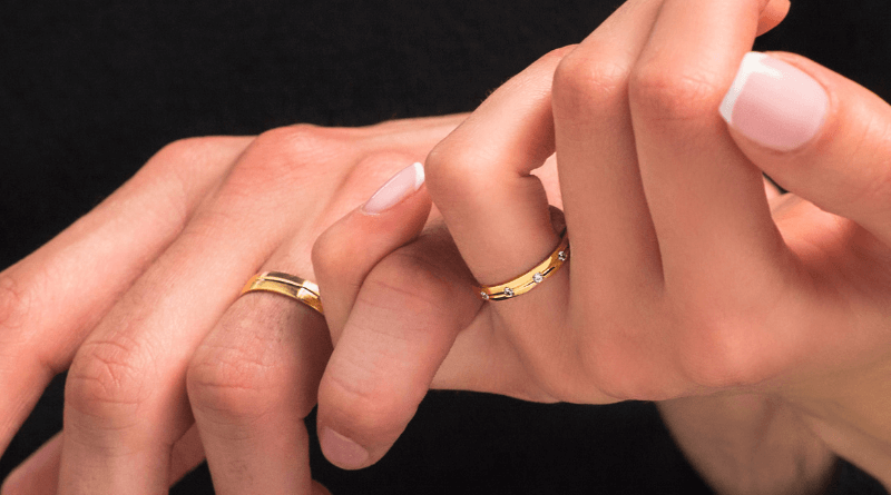 Par koji se drži za ruke noseći zlatno vjenčano prstenje s detaljem dijamanta