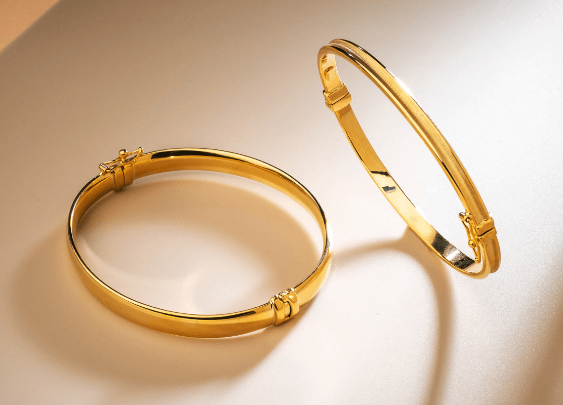 Dvije sjajne zlatne narukvice koje leže na stolu, spremne za nošenje i dodaju dašak elegancije svakoj odjeći.