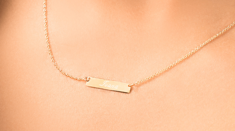 woman wearing gold necklace with bar that has name engraved on 